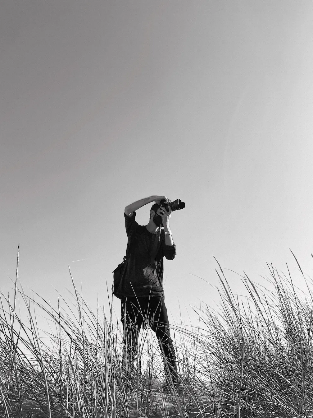 Ein Mann fotografiert inmitten von hohem Gras.