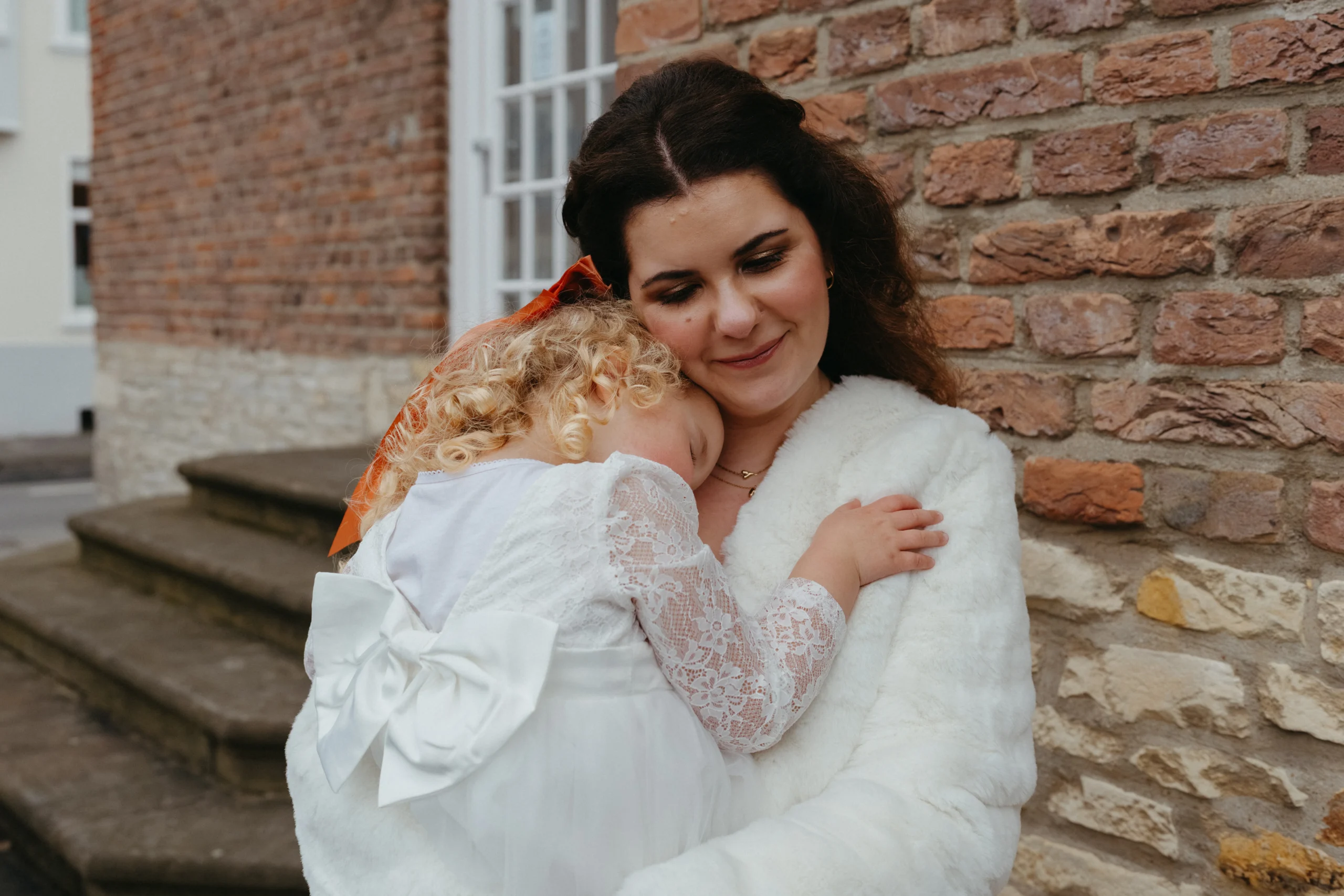 Bride hugging flower girl during wedding portrait outside historic building in Germany
