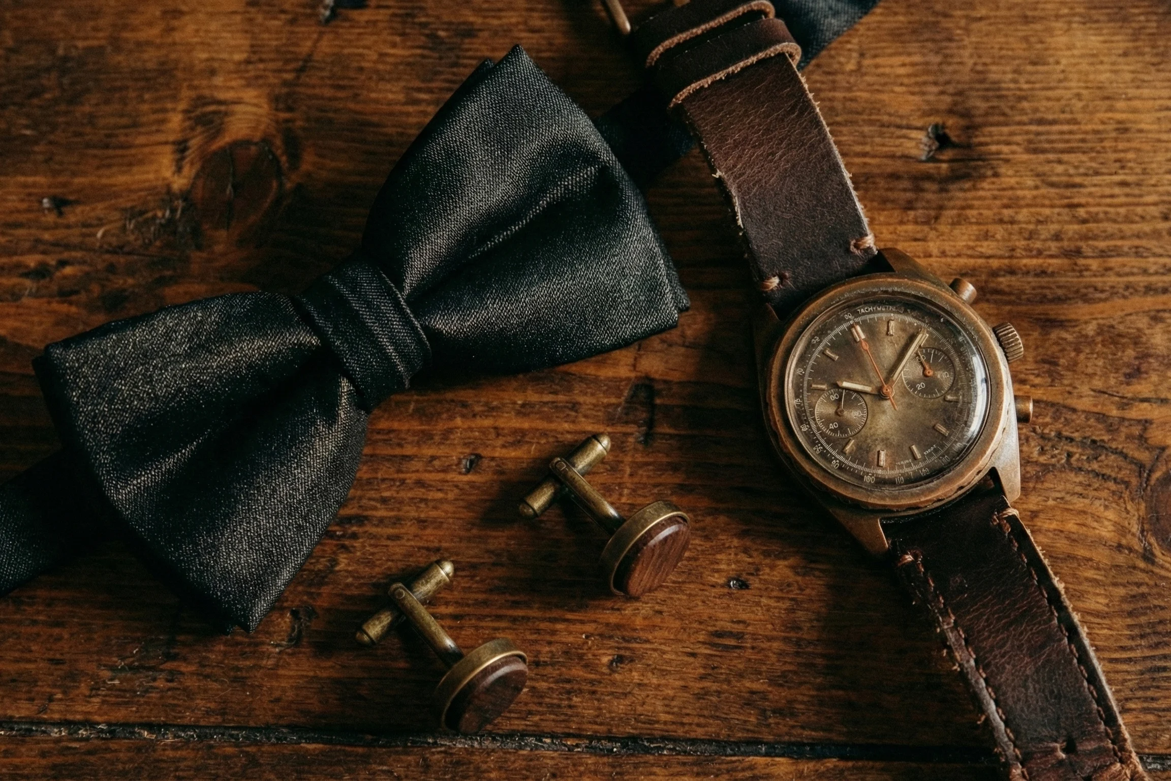Elegant groom accessories including bowtie watch and cufflinks photographed on rustic wooden table in Bavaria Germany