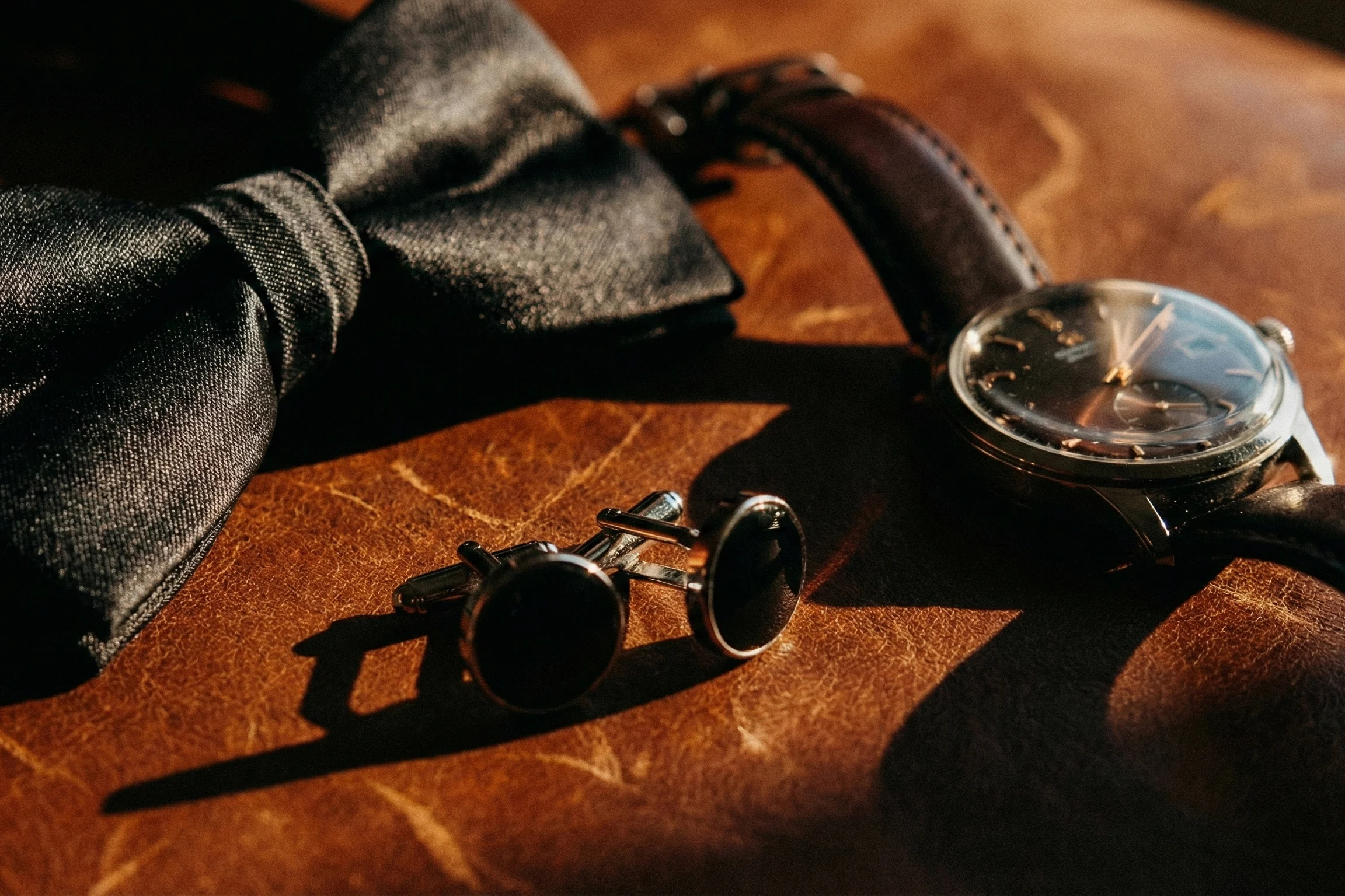 Moody wedding groom accessories including black bowtie wristwatch and cufflinks photographed in dramatic light