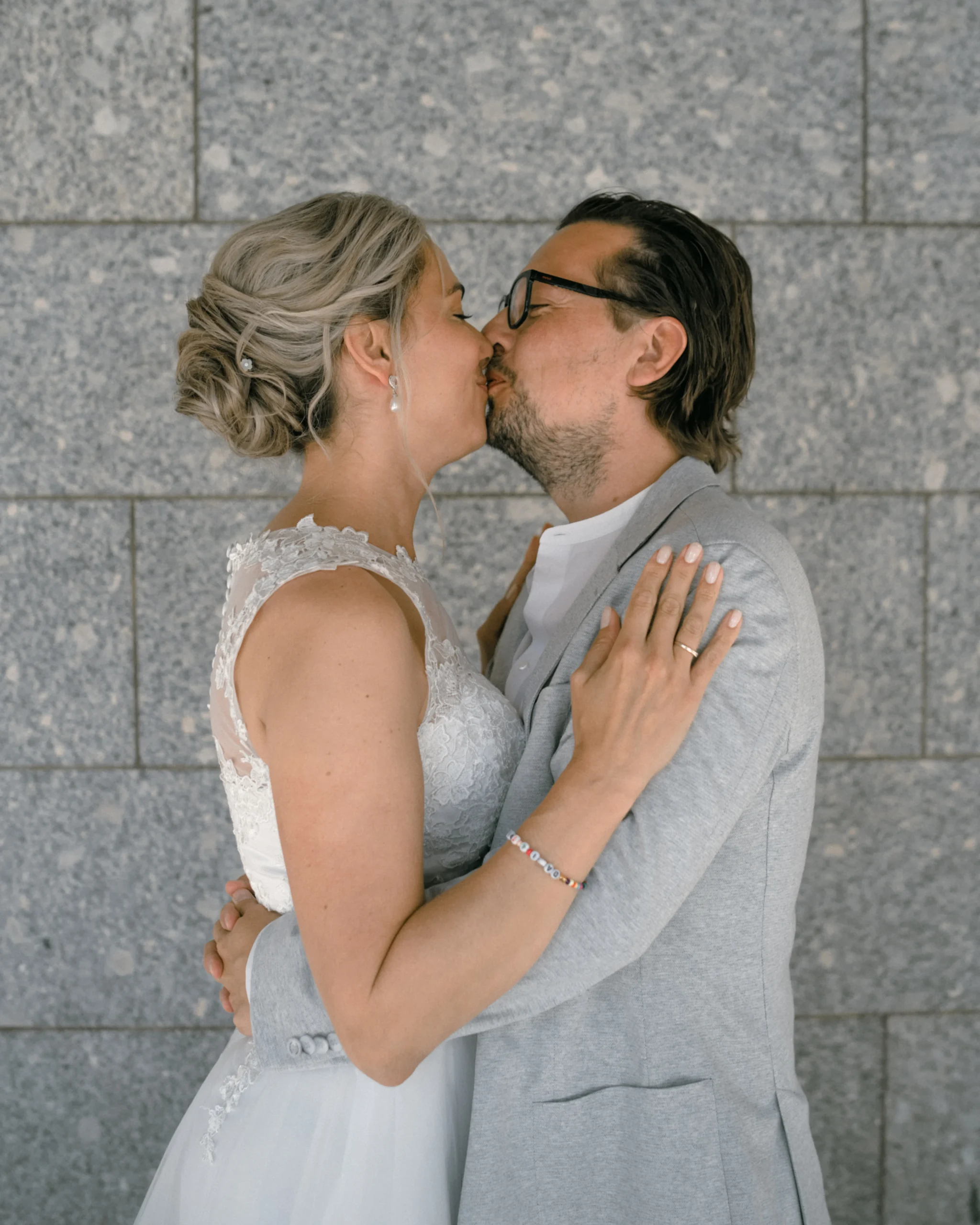 Brautpaar küsst sich vor einer modernen grauen Steinwand in Köln, künstlerisches Hochzeitsfoto.