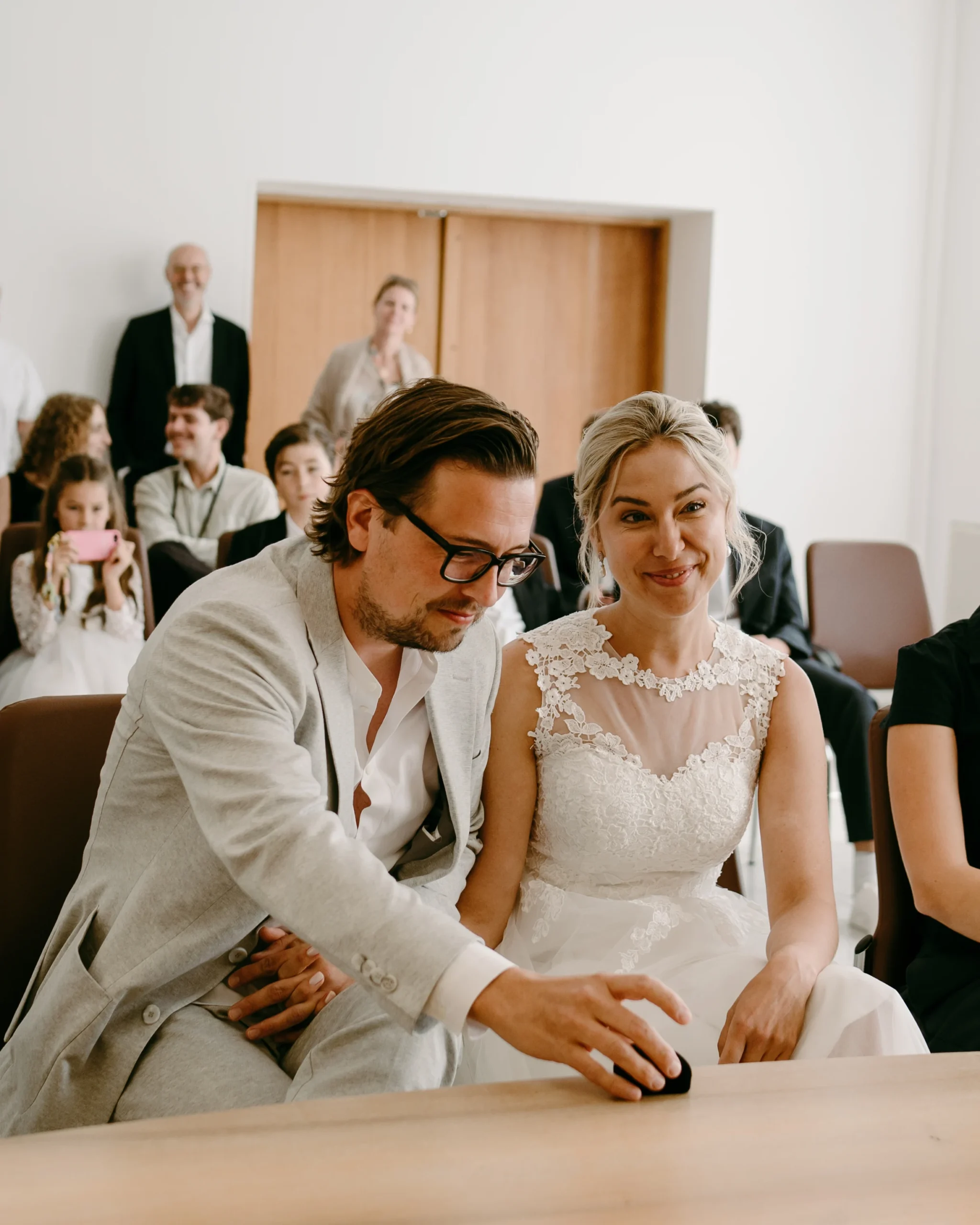 Nahaufnahme des Bräutigams, der während der standesamtlichen Trauung im Kölner Standesamt nach den Eheringen greift, mit der lächelnden Braut an seiner Seite.