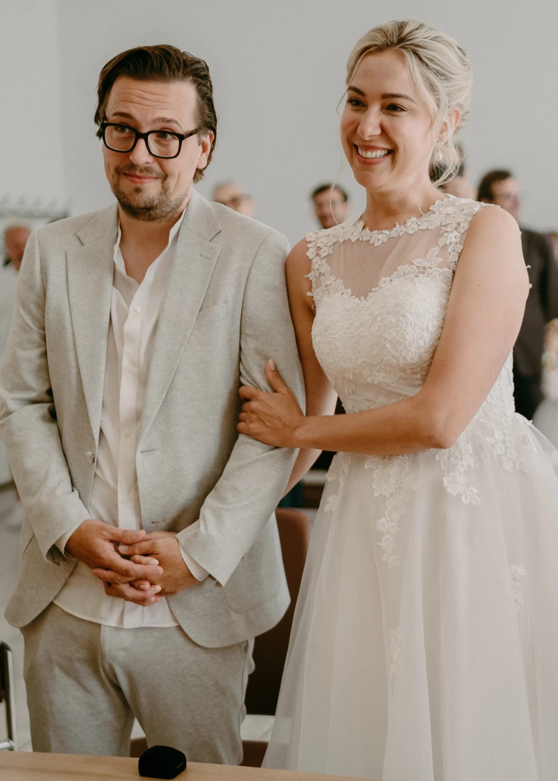 Draufsicht auf die offizielle Eheurkunde im Kölner Standesamt, während eine Trauzeugin ihre Unterschrift leistet, mit der Standesbeamtin im Hintergrund.