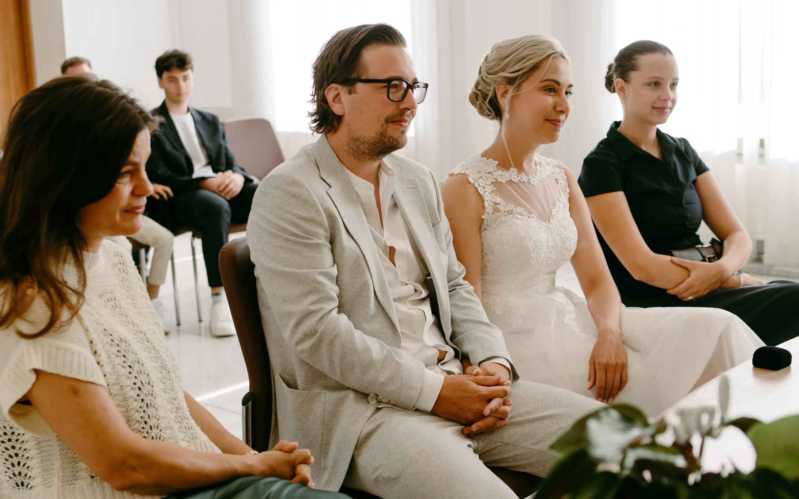 Seitenansicht von Braut und Bräutigam während der Zeremonie im Standesamt Köln, im Hintergrund die Trauzeugen in einem lichtdurchfluteten modernen Raum.