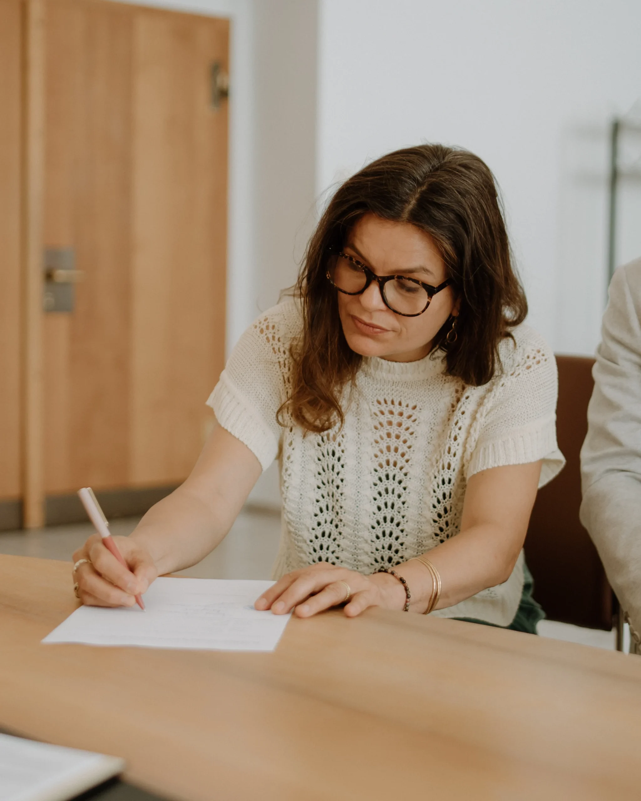 Hochzeitszeugin unterschreibt das Trauregister im Standesamt Köln während der standesamtlichen Trauung, Nahaufnahme mit Fokus auf die Unterschrift und die Zeugin mit Brille.